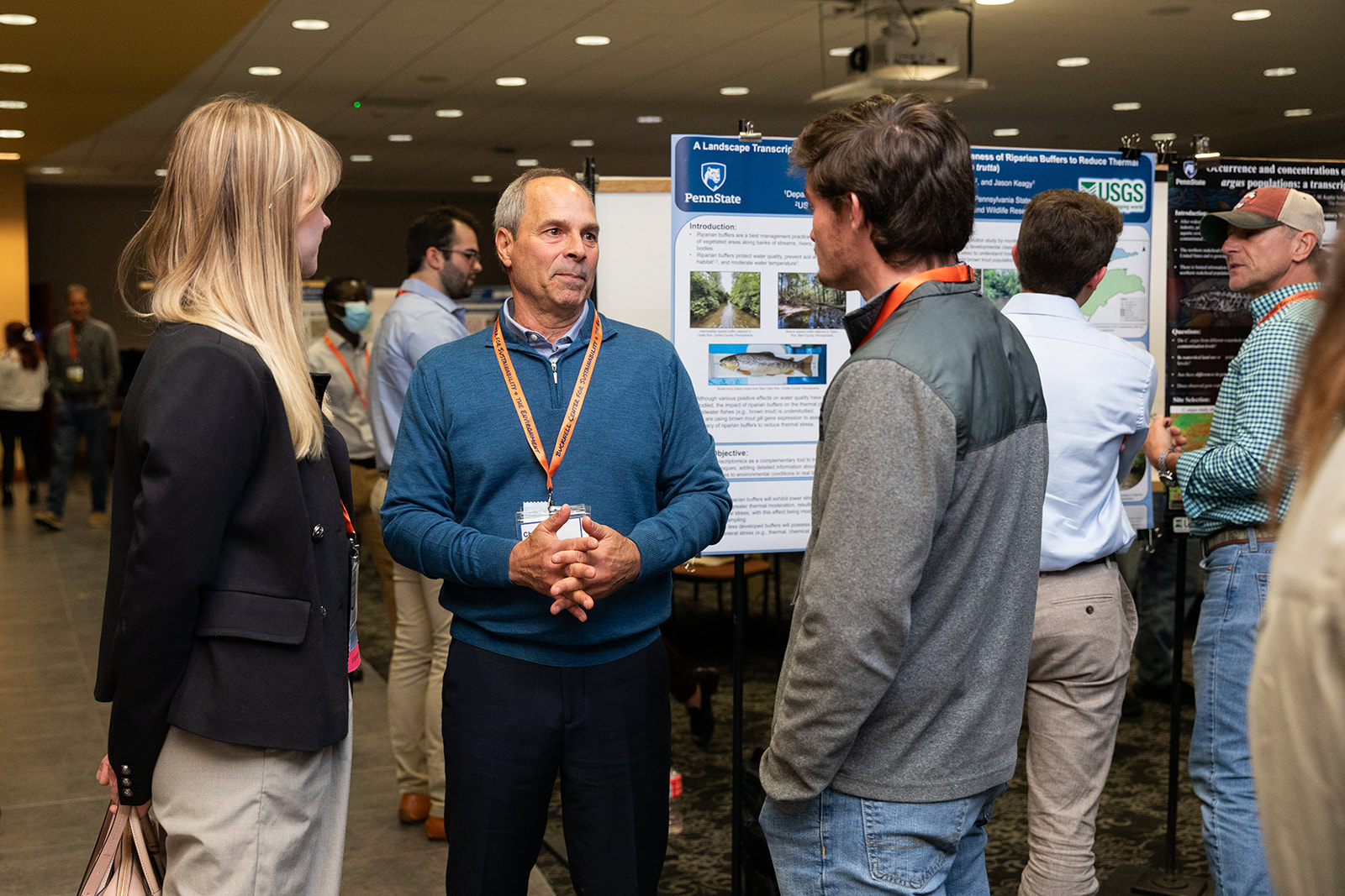 People standing around an academic poster, one presenting and several listening.