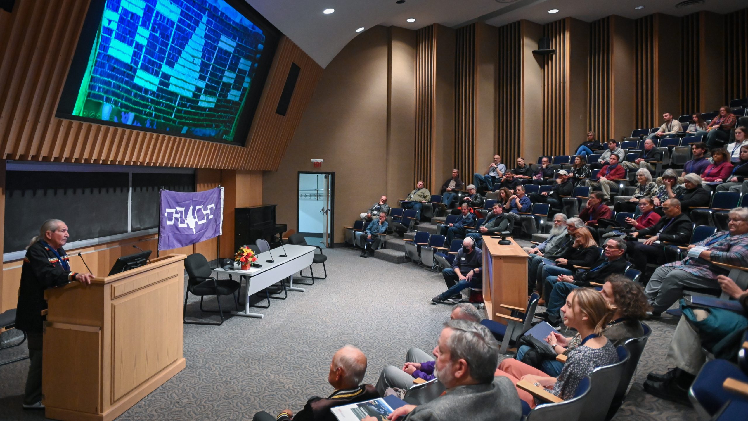 People standing around an academic poster, one presenting and several listening.