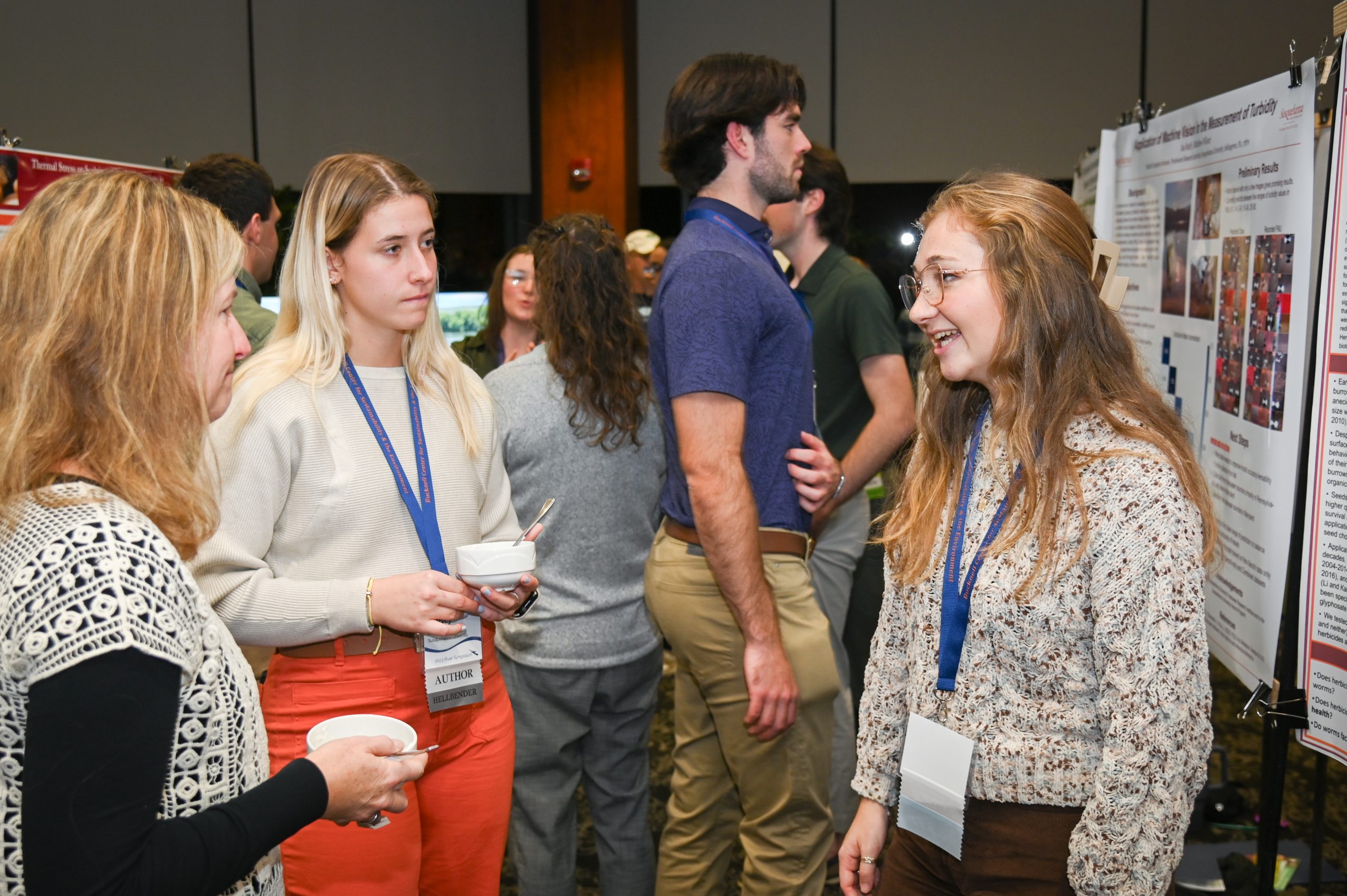 People standing around an academic poster, one presenting and several listening.
