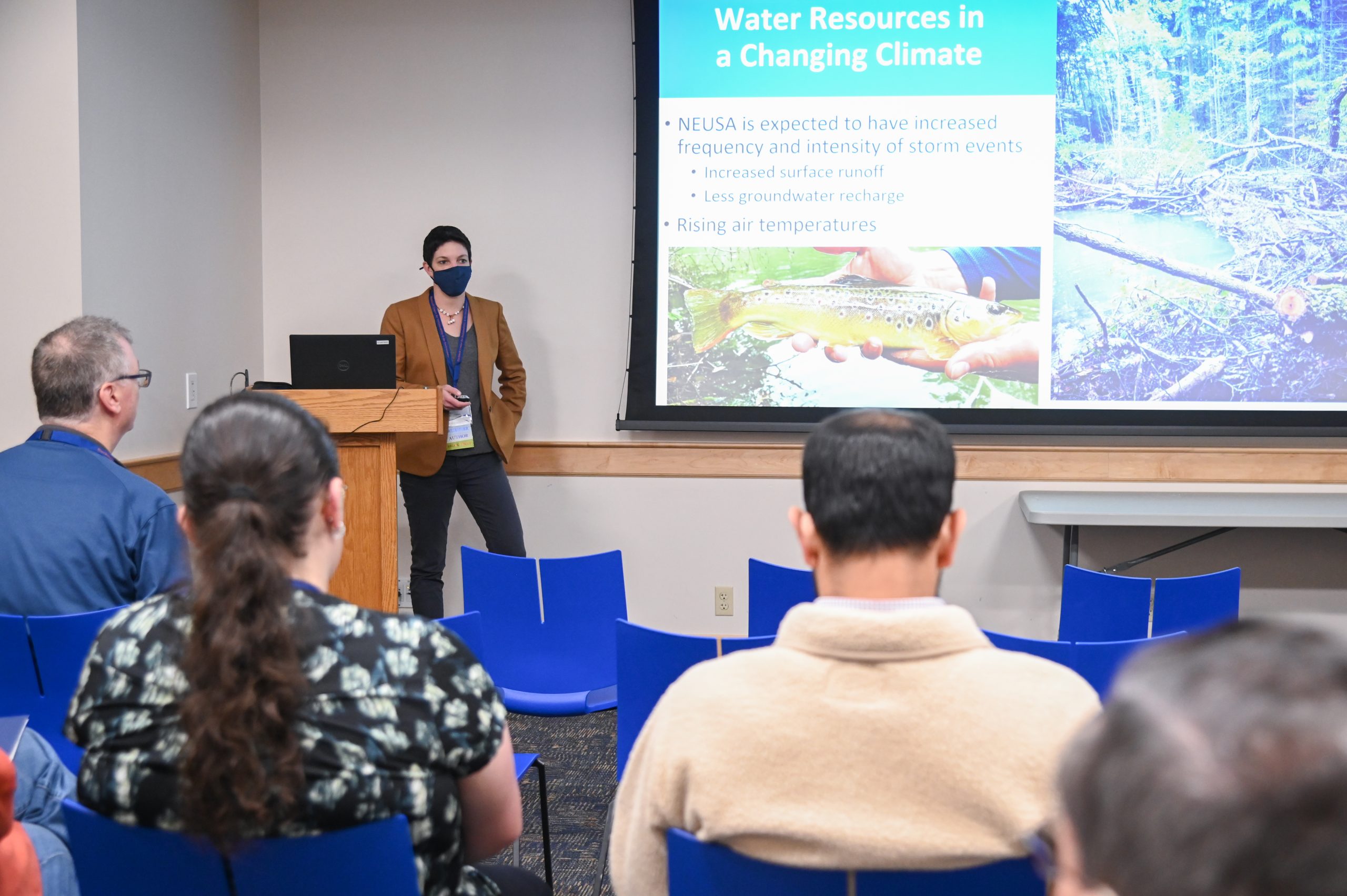 People standing around an academic poster, one presenting and several listening.